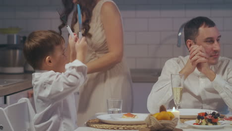 The-boy-asks-for-a-cake-in-the-holiday.-A-boy-of-3-5-years-laughs-and-demands-a-cake-at-the-holiday-table.-Shout-congratulations-and-ask-for-food.-High-quality-4k-footage